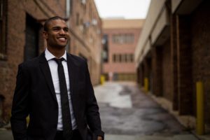 Man in a black suit and tie in an alley between two buildings